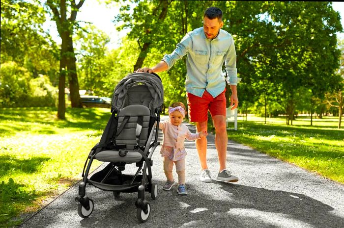 A joyful father with a child in a stroller enjoying a summer day in a Sydney park.