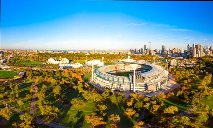 The iconic Melbourne skyline features the Melbourne Cricket Ground prominently against a cool autumn morning backdrop in Melbourne, Victoria, Australia.