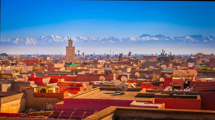 A panoramic view over red rooftops, scattered with satellite dishes, towards a sprawling mountain range in the distance