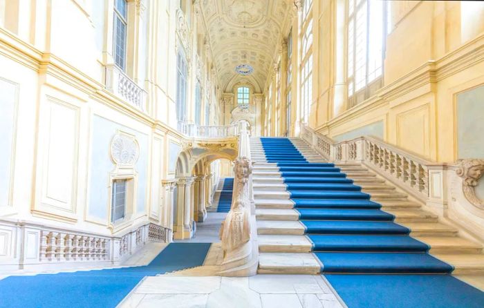 A grand white marble staircase adorned with blue carpets ascends through the space.