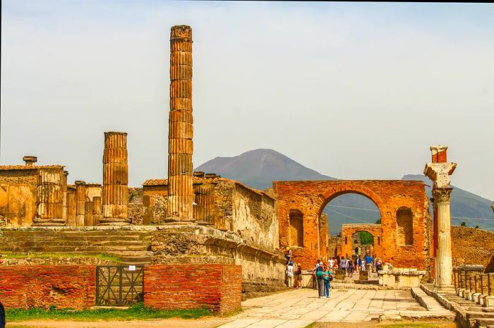 The ancient city of Pompeii. Visitors explore the ruins of this once-thriving city, which was obliterated by the eruption of Mt. Vesuvius, visible in the background.