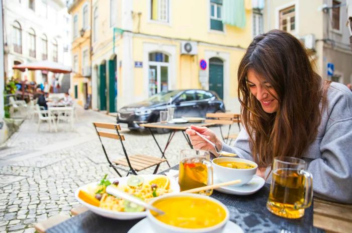 A tourist enjoying a traditional meal and drinks on a cozy terrace along a quaint street in Coimbra, Portugal.