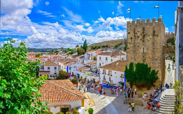 An aerial shot showcasing the medieval homes, walls, and tower of Óbidos, Portugal, bustling with crowds.