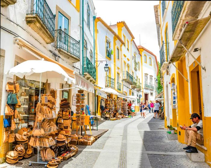 A street view of the Historic Centre of Évora, Portugal. The narrow streets are lined with stalls showcasing their goods outside.