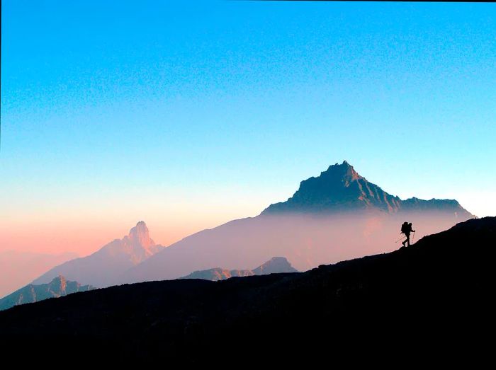 A hiker's silhouette with a backpack ascends a ridge in Gran Paradiso National Park at sunrise.