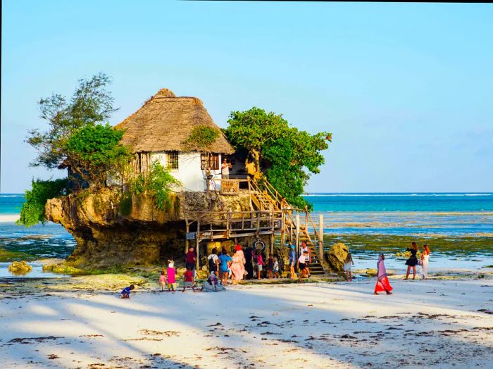 Groups of people gathered at The Rock, a restaurant perched on a cliff by Pingwe Beach in Zanzibar