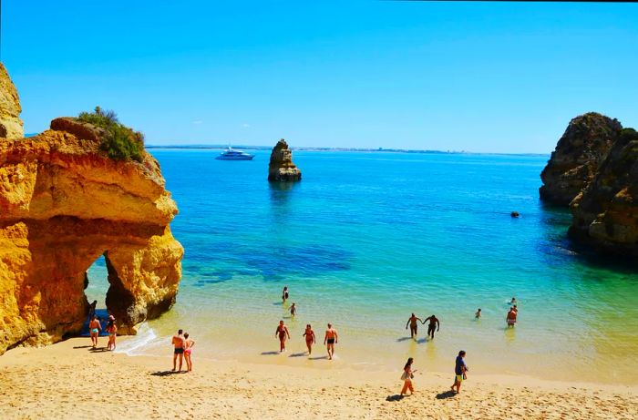 Visitors wade into the water at the picturesque Camilo Beach (Praia do Camilo) in the Algarve, Portugal, Europe.