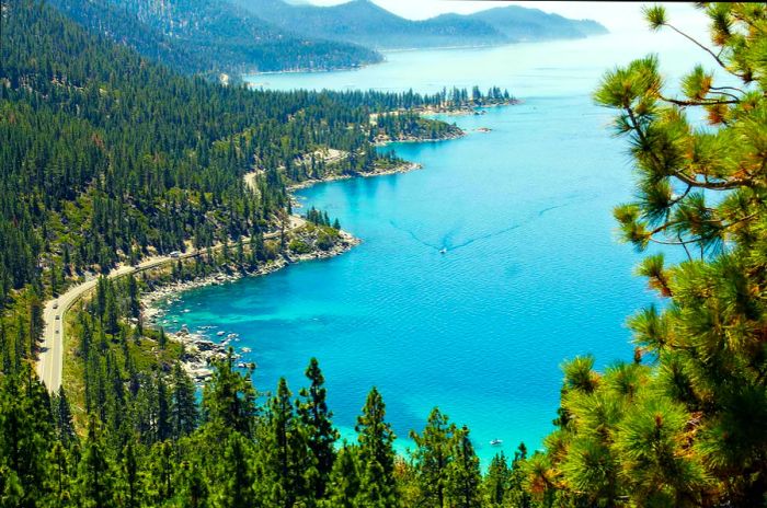 A boat glides across a shimmering lake with a road running beside it