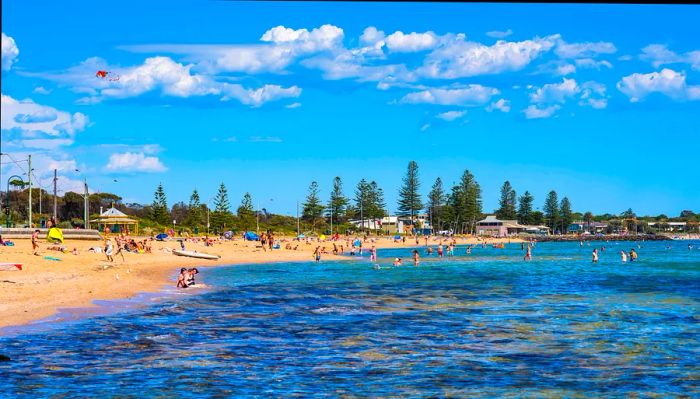 A beach scene featuring swimmers entering the water and sunbathers relaxing on the sand