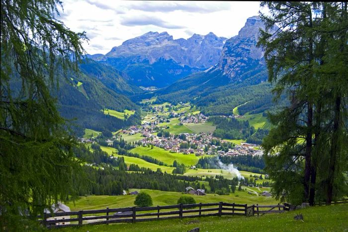 A panoramic view of La Villa, a quaint settlement set in a lush valley with the majestic Dolomites in the background.