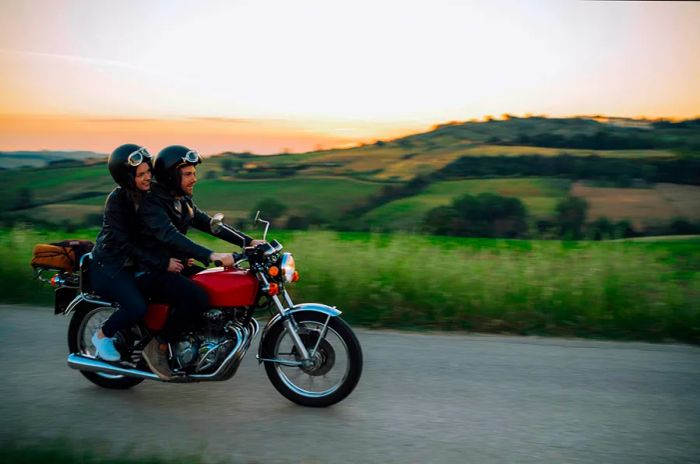 A couple rides on the back of a motorbike through the scenic Tuscan countryside as the sun sets.