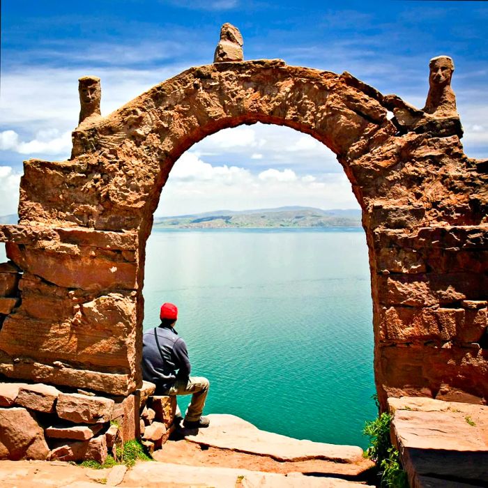 A man in a red hat relaxes beneath a stone archway on Taquile Island, Lake Titicaca, Peru