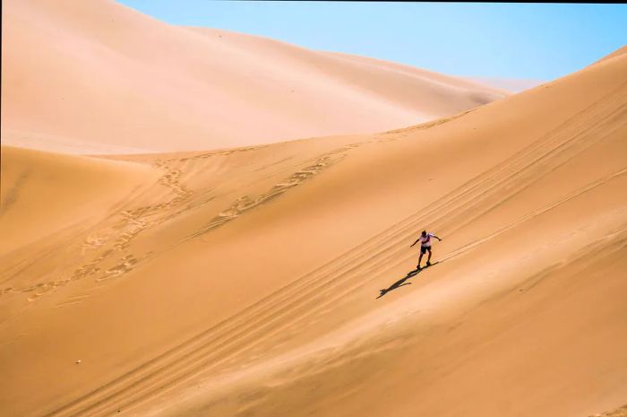 Silhouette of a person sandboarding on the dunes.