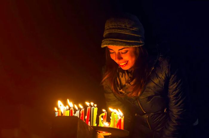 A joyful Colombian woman lighting candles outdoors during the Noche de Velitas celebration on December 7, marking the start of the Christmas season.