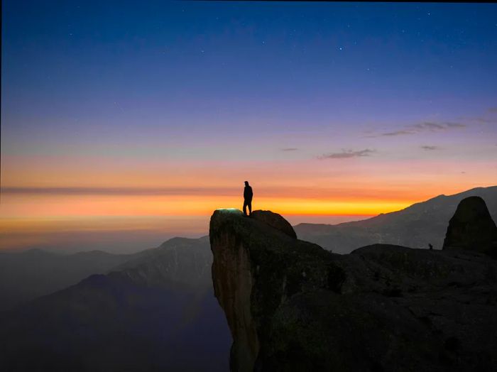 A lone figure gazes over a breathtaking view from Marcahuasi, a plateau nestled in the Andes Mountains during the evening light.