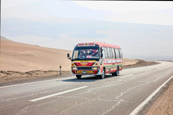 A brightly painted bus makes its way along the Pan-American Highway in Peru. Some passengers can be seen through the colorful windows, while the surrounding landscape features arid desert.