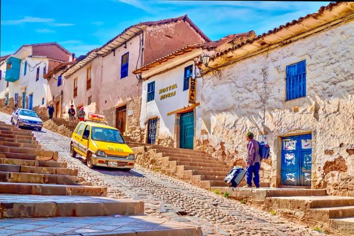 A taxi navigates a steep, cobbled street in the historic center of Cusco, where the buildings have been transformed into charming hotels.