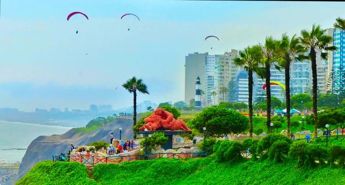 A view of paragliders soaring over the Park of Love with tourists gathering around the El Beso sculpture