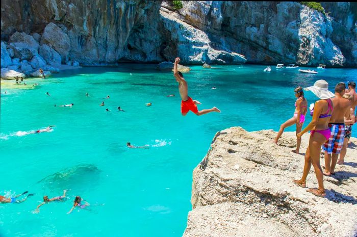 People leap off cliffs into the clear turquoise waters below.