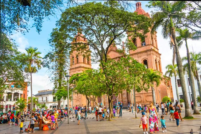 A vibrant plaza bustling with people in Santa Cruz de la Sierra, Bolivia, with the Basilica de San Lorenzo gracing the background.