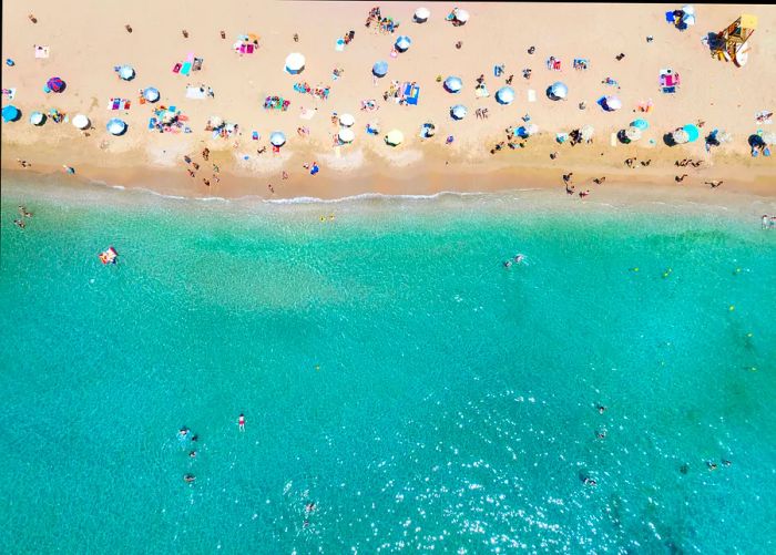 An aerial view showcasing a turquoise sea with beachgoers in Athens, Greece