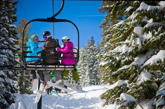 Three cheerful skiers enjoying a chair lift on a sunny day at Palisades Tahoe (Squaw Valley), California, USA