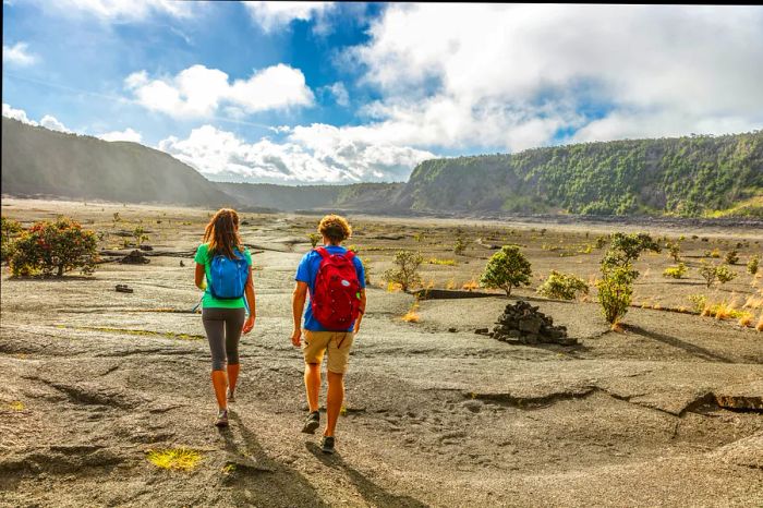 Two hikers head away from the camera along a hiking trail that stretches across a vast, dusty crater.