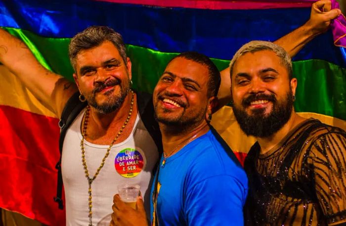 Three men joyfully carrying a pride flag in Rio de Janeiro, Brazil