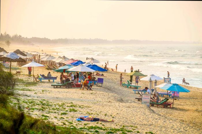 Visitors enjoying An Bang beach in Hoi An, where golden sands meet the blue waves, filled with a lively crowd.