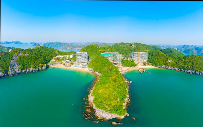 An aerial view capturing two beaches on Cat Ba island, where new constructions are underway along the shoreline. Both water and sky display a lovely blue hue.