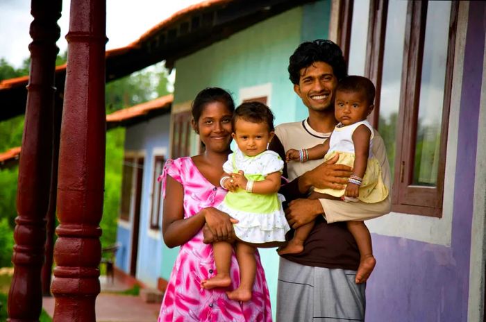 A Sri Lankan family featuring a woman, man, and two small children, all smiling at the camera.