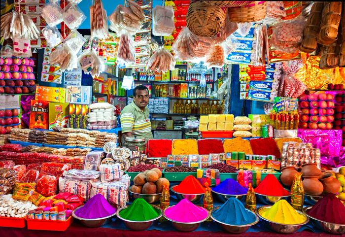 A man surrounded by vibrant goods at a small market stall in Delhi.