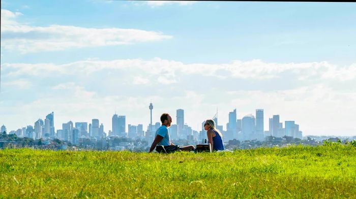 A couple relaxing in a field with Sydney's skyline towering in the background