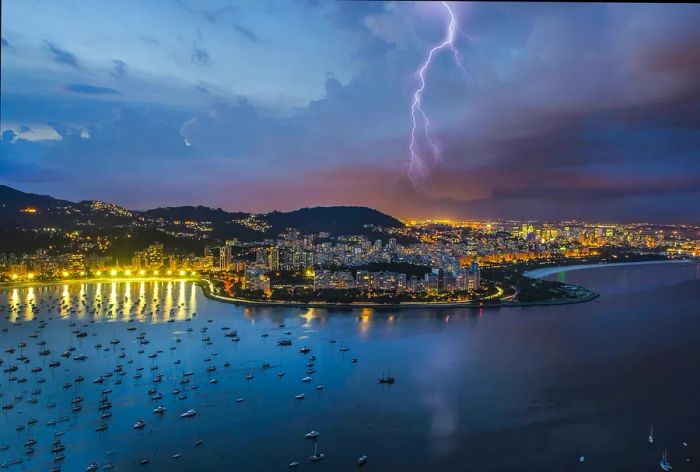 A flash of lightning streaks across a stormy sky over a coastal city