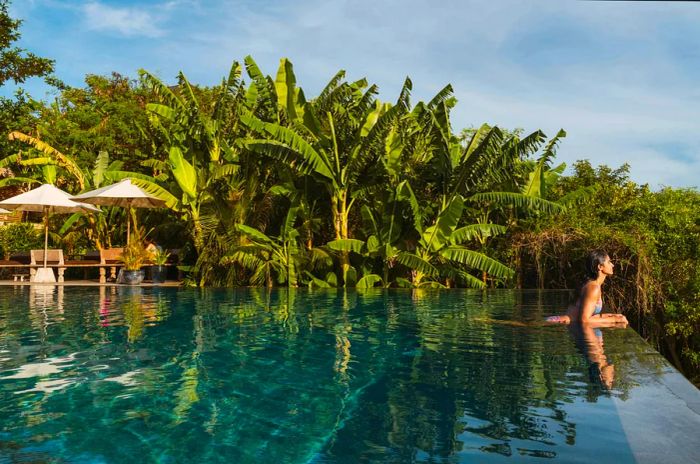 Wide panoramic view of a woman relaxing by a breathtaking infinity pool resort surrounded by palm trees on Lombok island