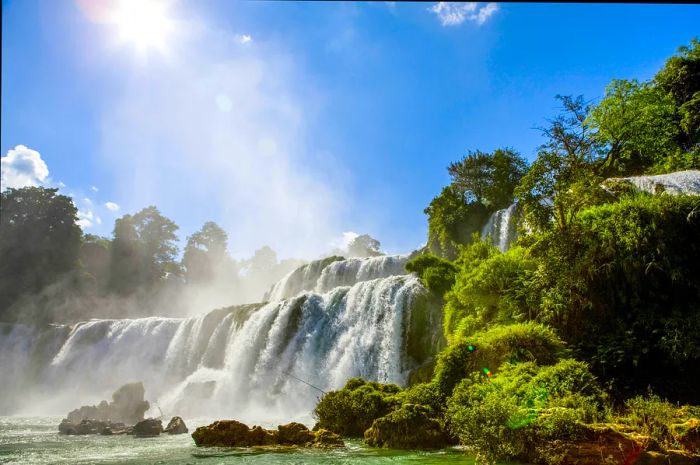 The Ban Gioc Waterfalls surrounded by lush greenery on a sunny day.