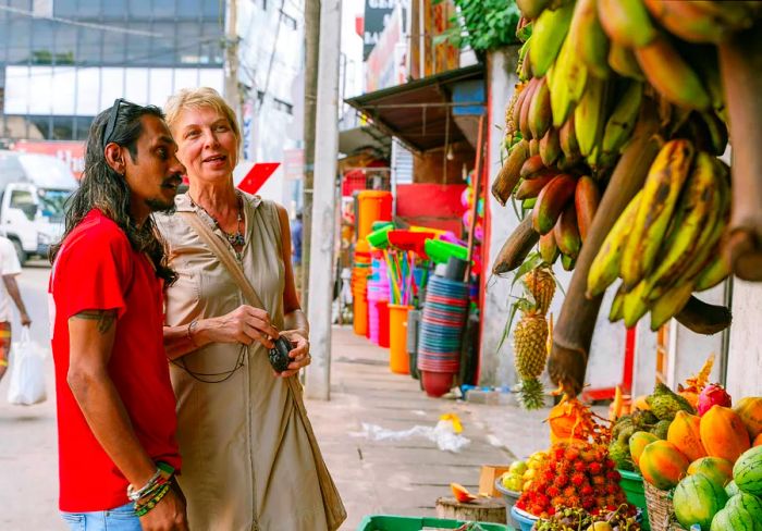 A young Sri Lankan man and an older white woman are seen at a fruit stall in the city.