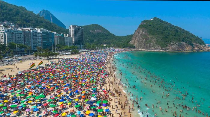 A bustling beach filled with people seeking shade under vibrant umbrellas