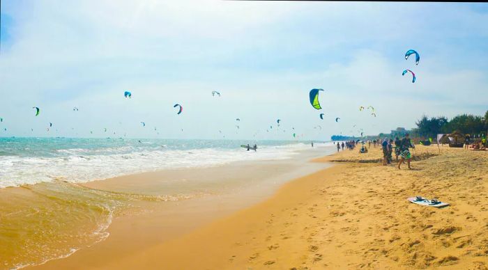 Mui Ne beach in Vietnam features a long stretch of white sand, with colorful kites of kite surfers dotting the sky above.