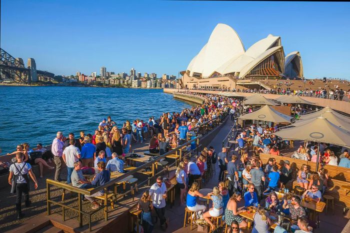 People enjoy socializing at picnic tables on a rooftop overlooking the harbor