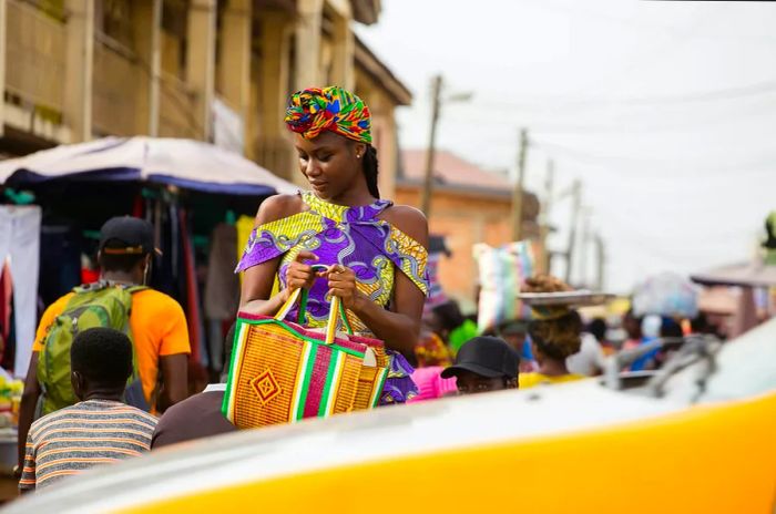 A young woman strolls through a bustling market in Accra, Ghana, as a taxi drives by.