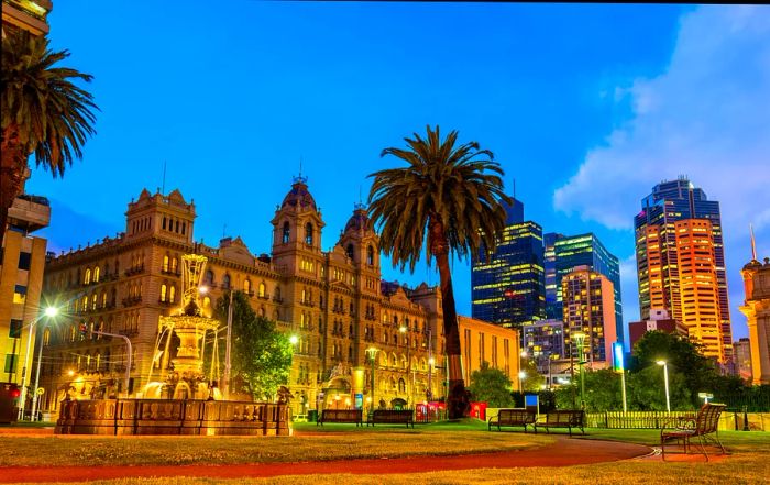 A stunning view of Parliament House alongside its garden in Melbourne, Australia. The impressive building is beautifully illuminated during the evening hours.