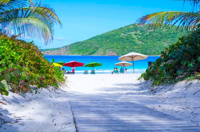 A sandy boardwalk dusted with fine white sand stretches down to a beach where visitors unwind beneath vibrant umbrellas on the island of Culebra, Puerto Rico.