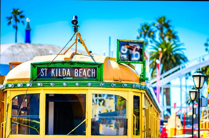 The upper part of a yellow Melbourne tram, displaying a destination card reading 'St Kilda', against a backdrop of a clear blue sky.