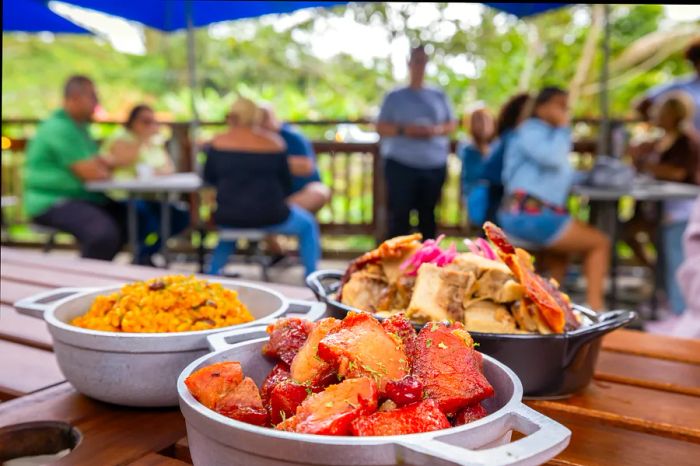 A delicious smoked meat dish served with rice and mac and cheese on a rustic wooden table in a bustling restaurant.