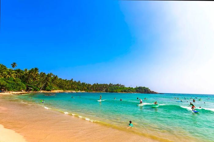 People riding waves at surf beach in Hiriketiya, Dikwella, Sri Lanka.