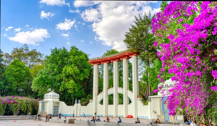 Individuals relaxing in a park adorned with a magnificent row of columns and vibrant fuchsia flowers