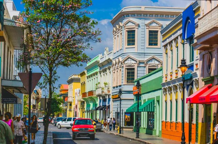 A red car cruises down a street adorned with pastel-colored buildings in the city of Ponce, Puerto Rico.