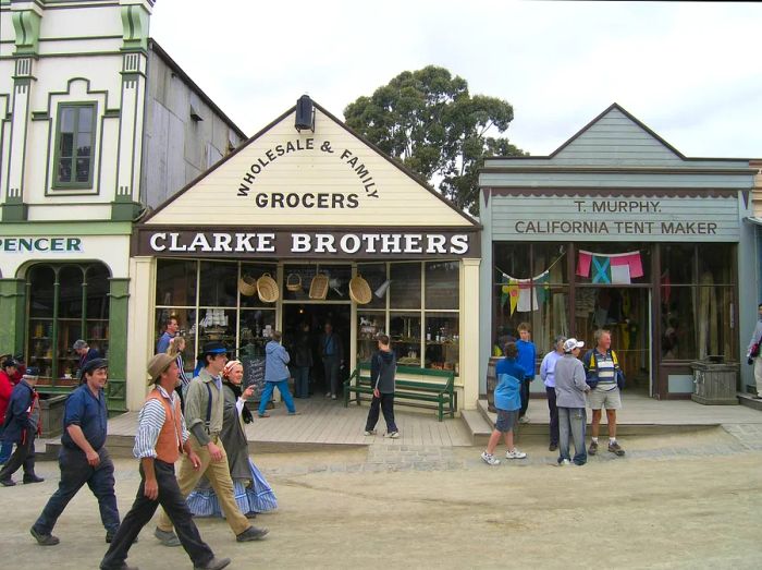 An old-fashioned town featuring storefronts like Clarke Brothers Wholesale & Family Grocers and T. Murphy California Tent Maker.