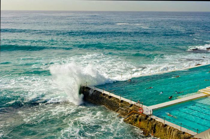 A wave crashes over the edge of a man-made swimming pool